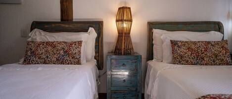 A room with two beds, each with a patterned pillow and a small wooden nightstand between them.