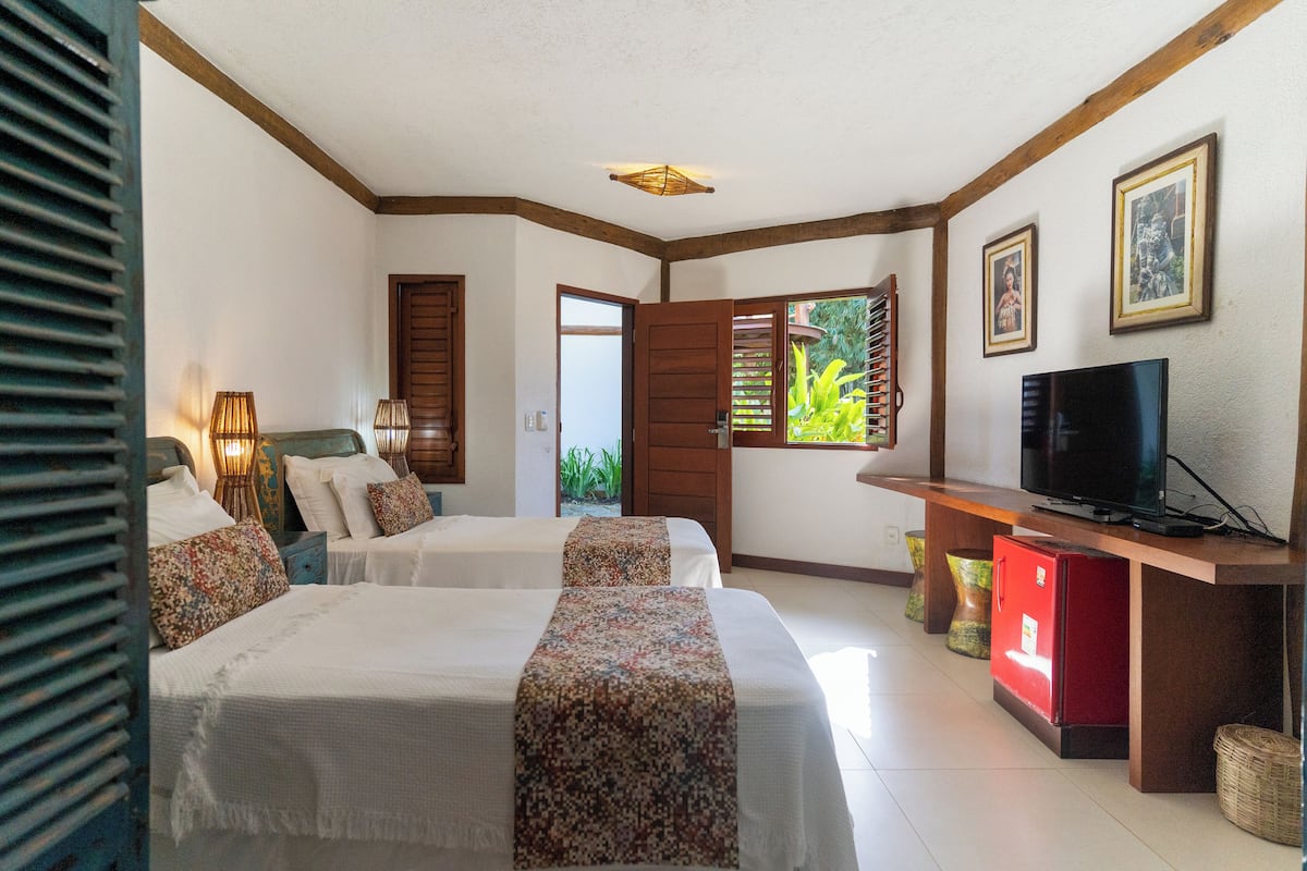 Habitación de hotel con dos camas, televisor, refrigerador pequeño y ventana con vista a zonas verdes.