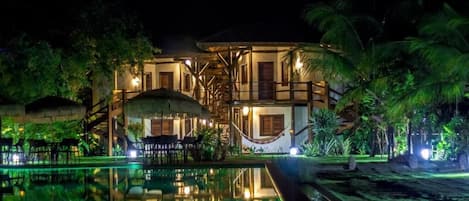 A hotel with a pool, outdoor seating, and tropical vegetation.