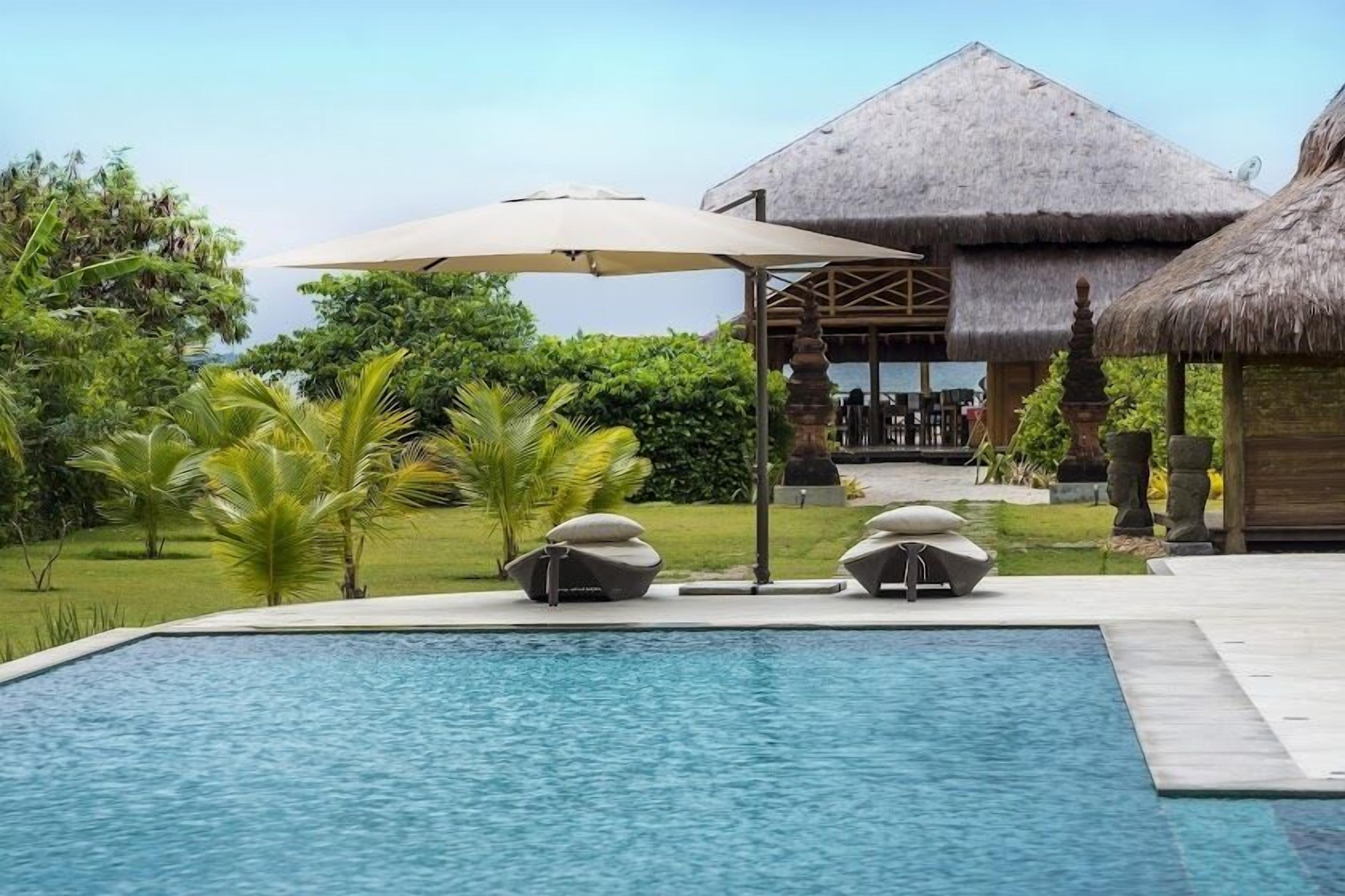 A swimming pool with lounge chairs and a thatched-roof structure in the background.