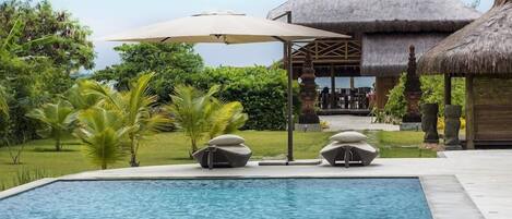 A swimming pool with lounge chairs and a thatched-roof structure in the background.