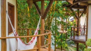 A wooden deck with a hammock, surrounded by lush green plants and bamboo trees. - Hotel Villa Balidendê (Maraú)