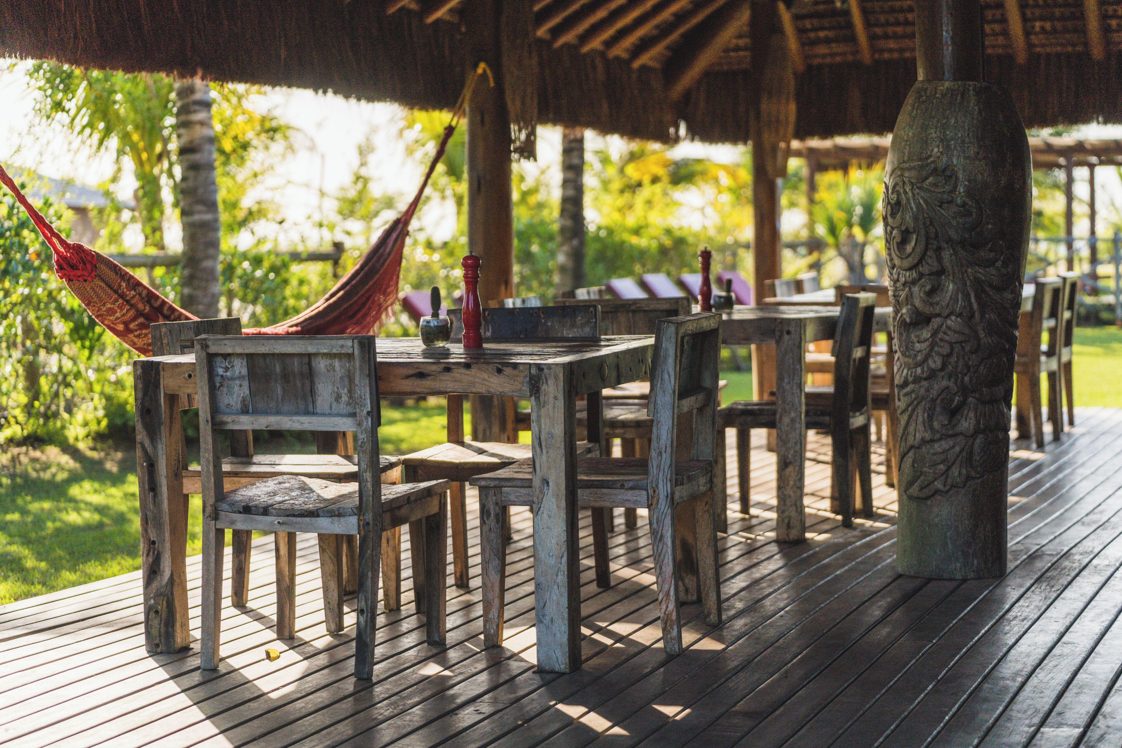 Una terraza de madera con mesas y sillas, una hamaca y un pilar decorativo.