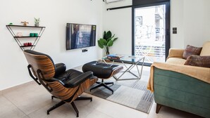 A modern living room with a green sofa, black leather chairs, a glass coffee table, and a TV mounted on the wall. - Beautiful Aparment in Psiri-Monastiraki (Athens)