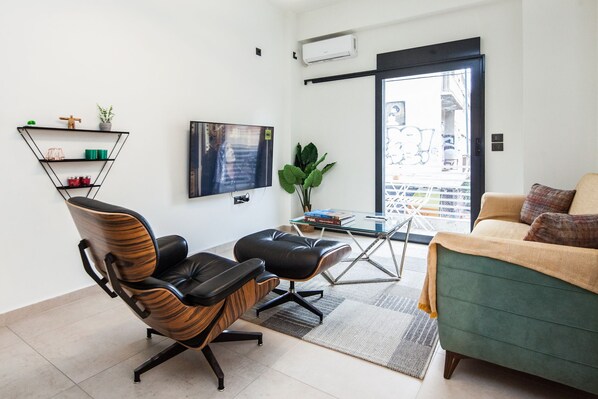 A modern living room with a green sofa, black leather chairs, a glass coffee table, and a TV mounted on the wall.