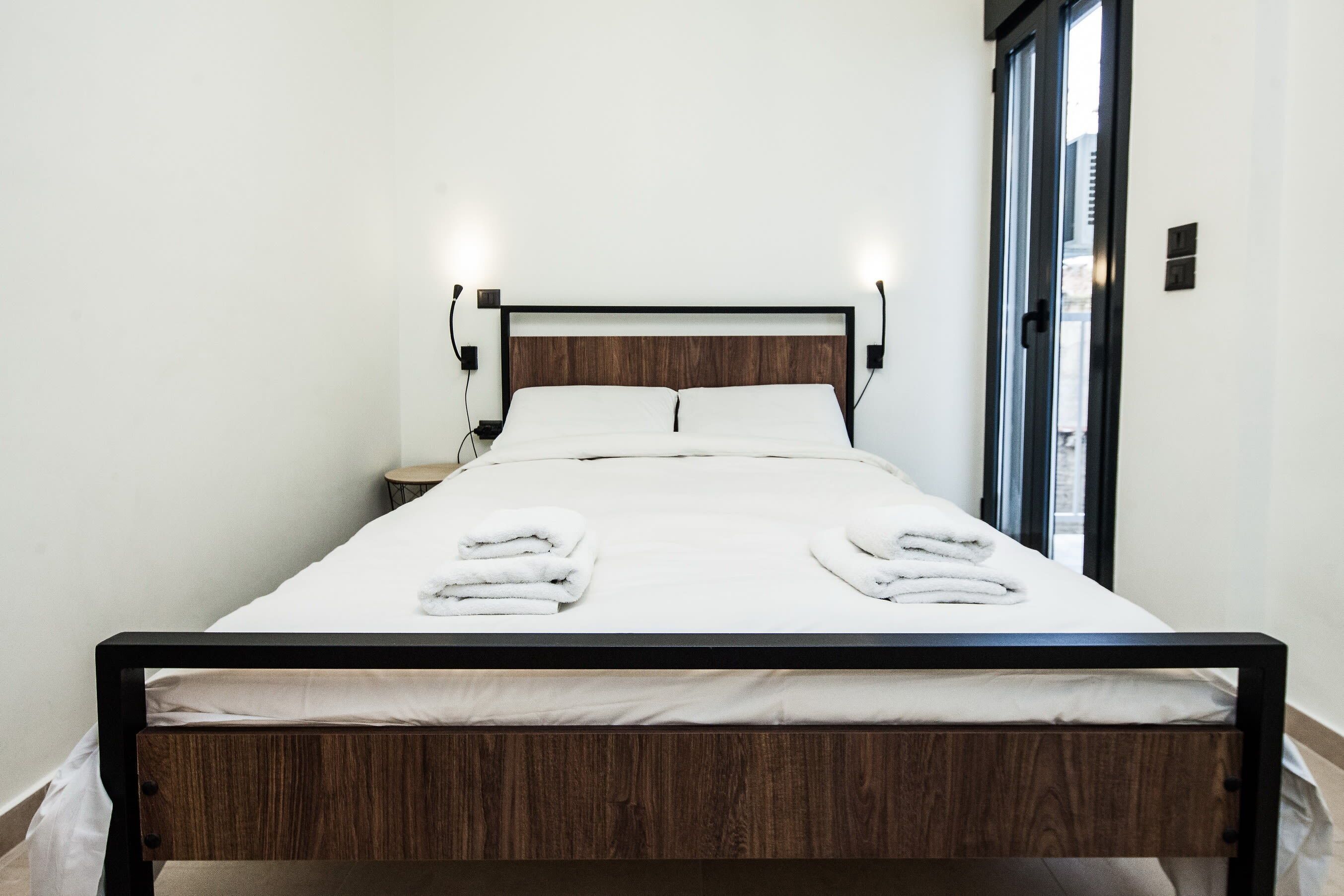 A neatly made bed with white linens and towels, a wooden headboard, and bedside lamps.