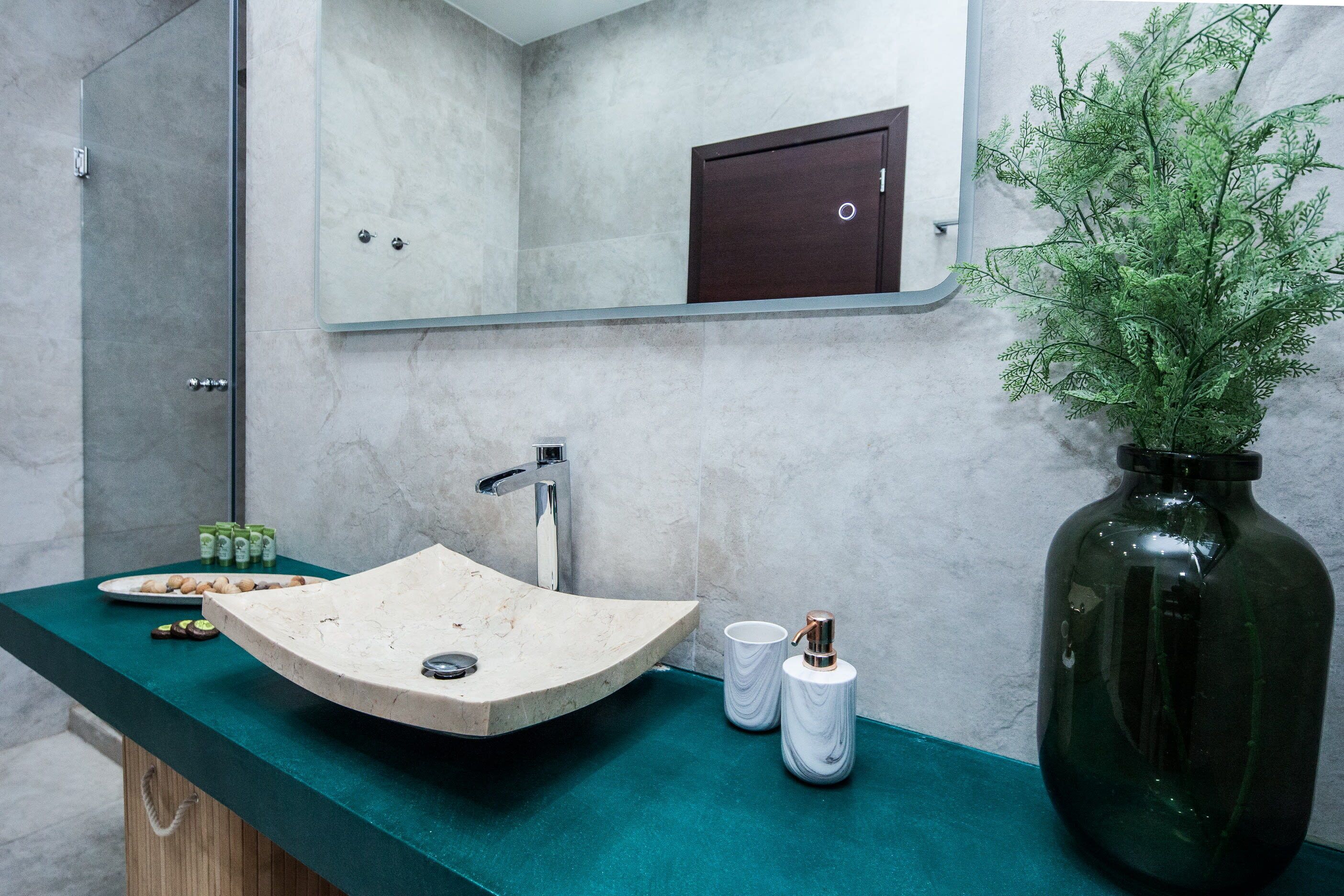 A bathroom with a curved sink, a mirror, a dark wooden cabinet, and a green countertop.