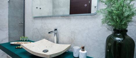 A bathroom with a curved sink, a mirror, a dark wooden cabinet, and a green countertop.