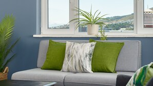 Een moderne woonkamer met een grijze bank, een zwarte salontafel en uitzicht op een stadslandschap door een groot raam.