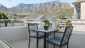 Een balkon met een tafel en stoelen, met uitzicht op een stad en een berg.