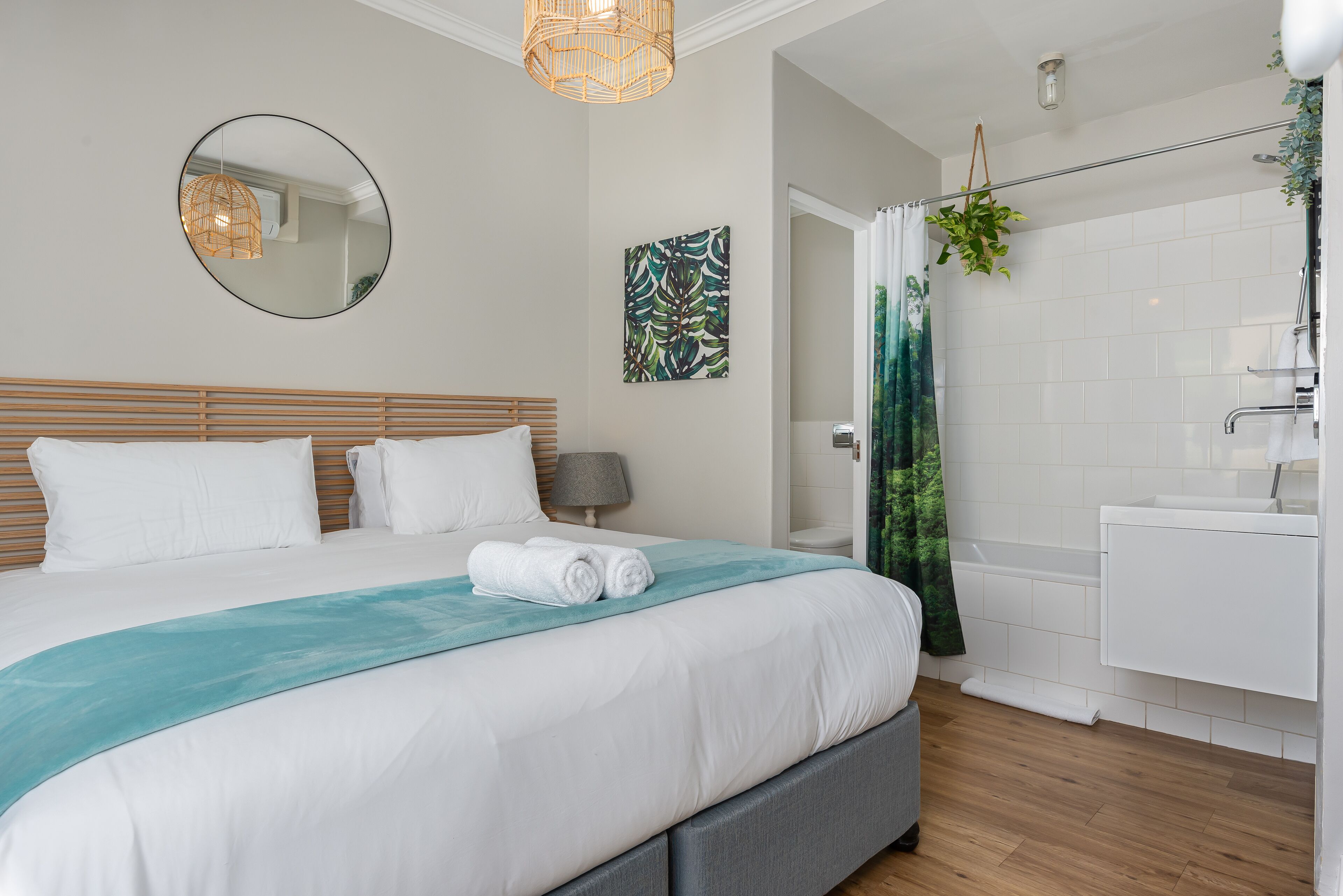 A modern bedroom with a large bed, a bedside table, a mirror, and a view into the bathroom.