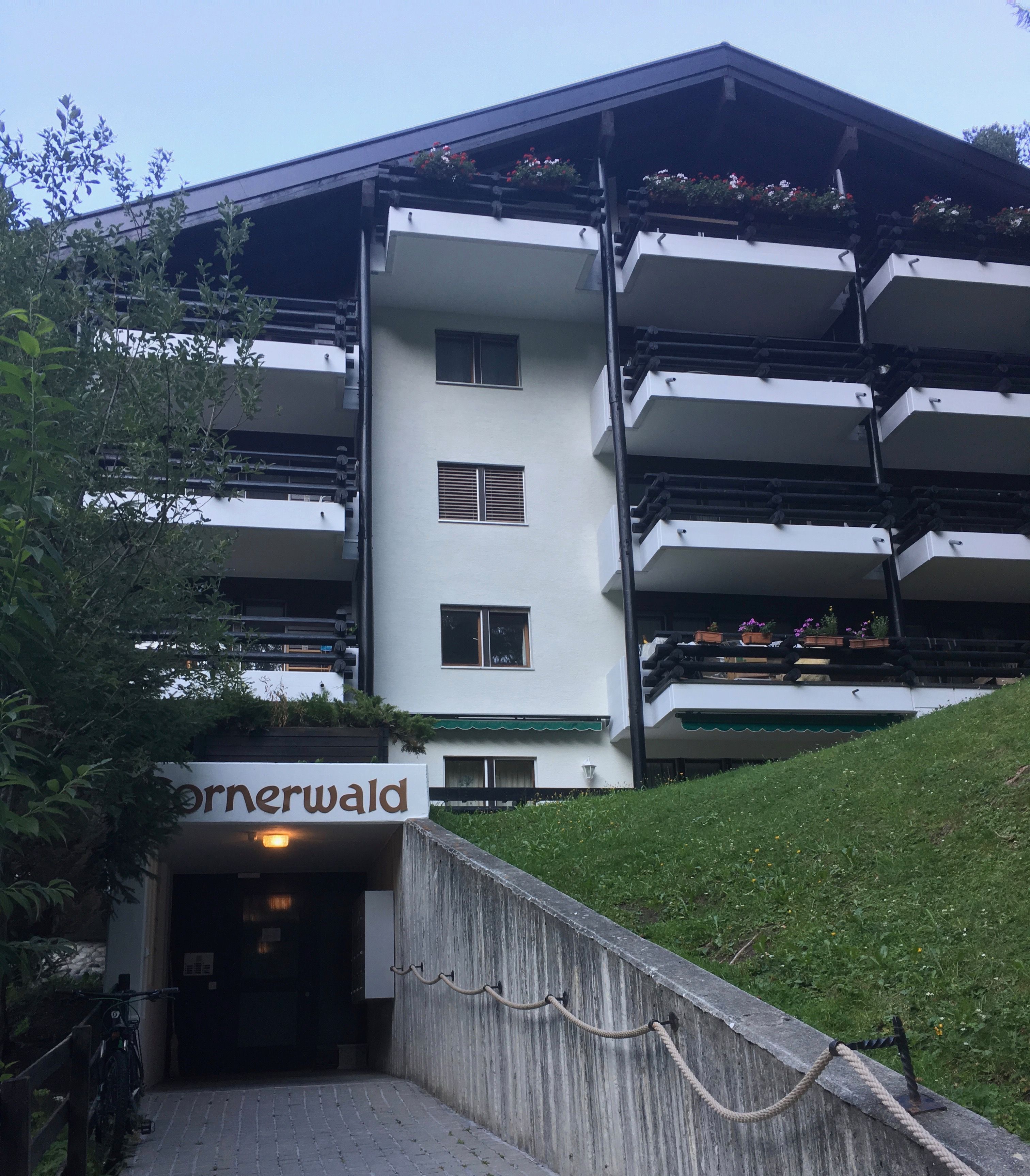 A multi-story building with balconies, a sign reading "Cornerwald," and a paved entrance area.