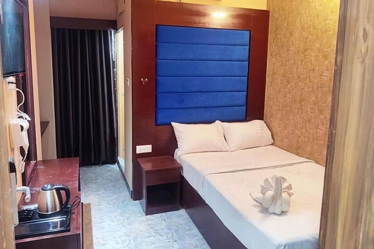 A compact hotel room with a bed, a small table with a kettle, and a built-in air conditioner.