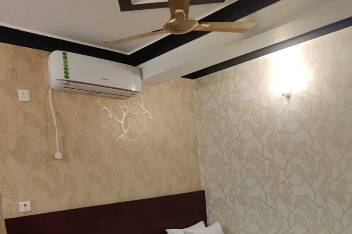 A hotel room with two single beds, a ceiling fan, an air conditioning unit, and patterned wallpaper.