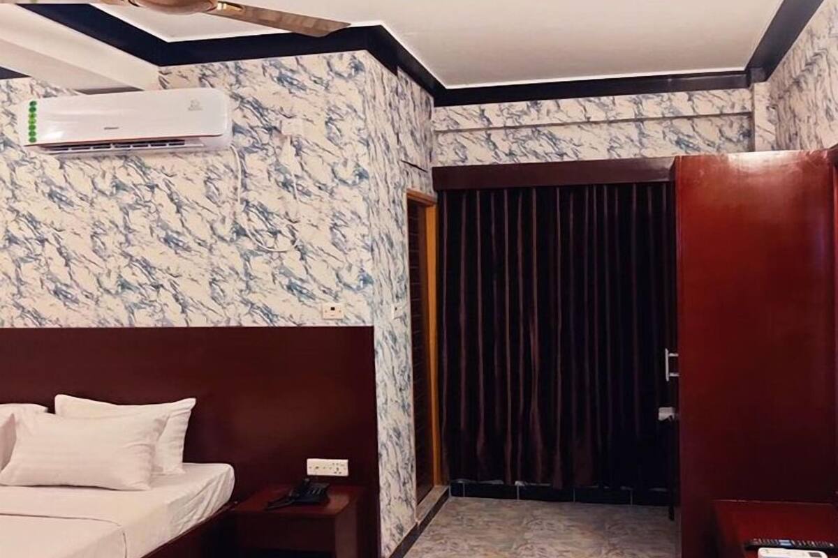 A hotel room with a bed, bedside table, and an air conditioning unit.