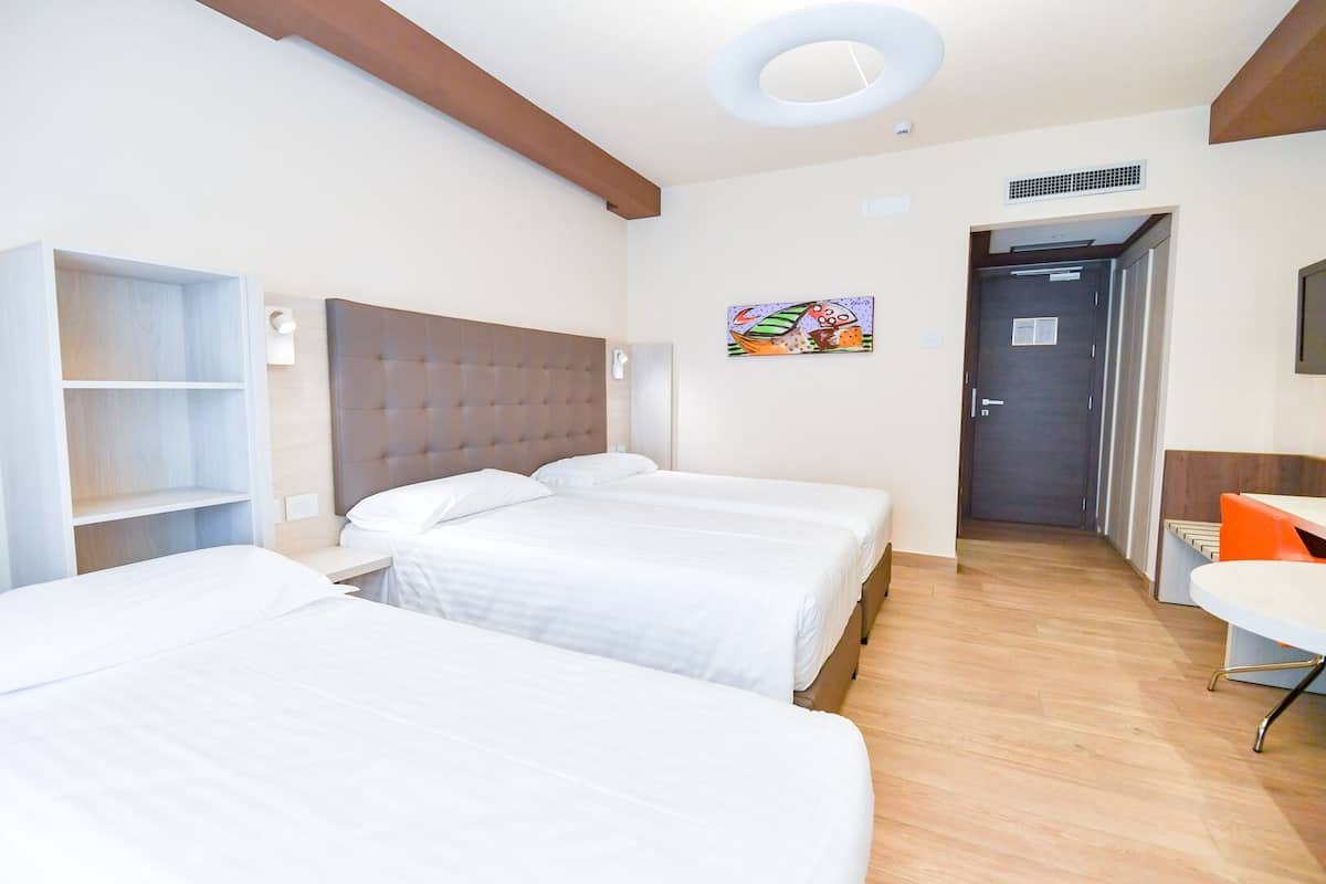 Habitación de hotel con dos camas, un escritorio y una silla. Hay un cuadro en la pared y una puerta que da a otra habitación.