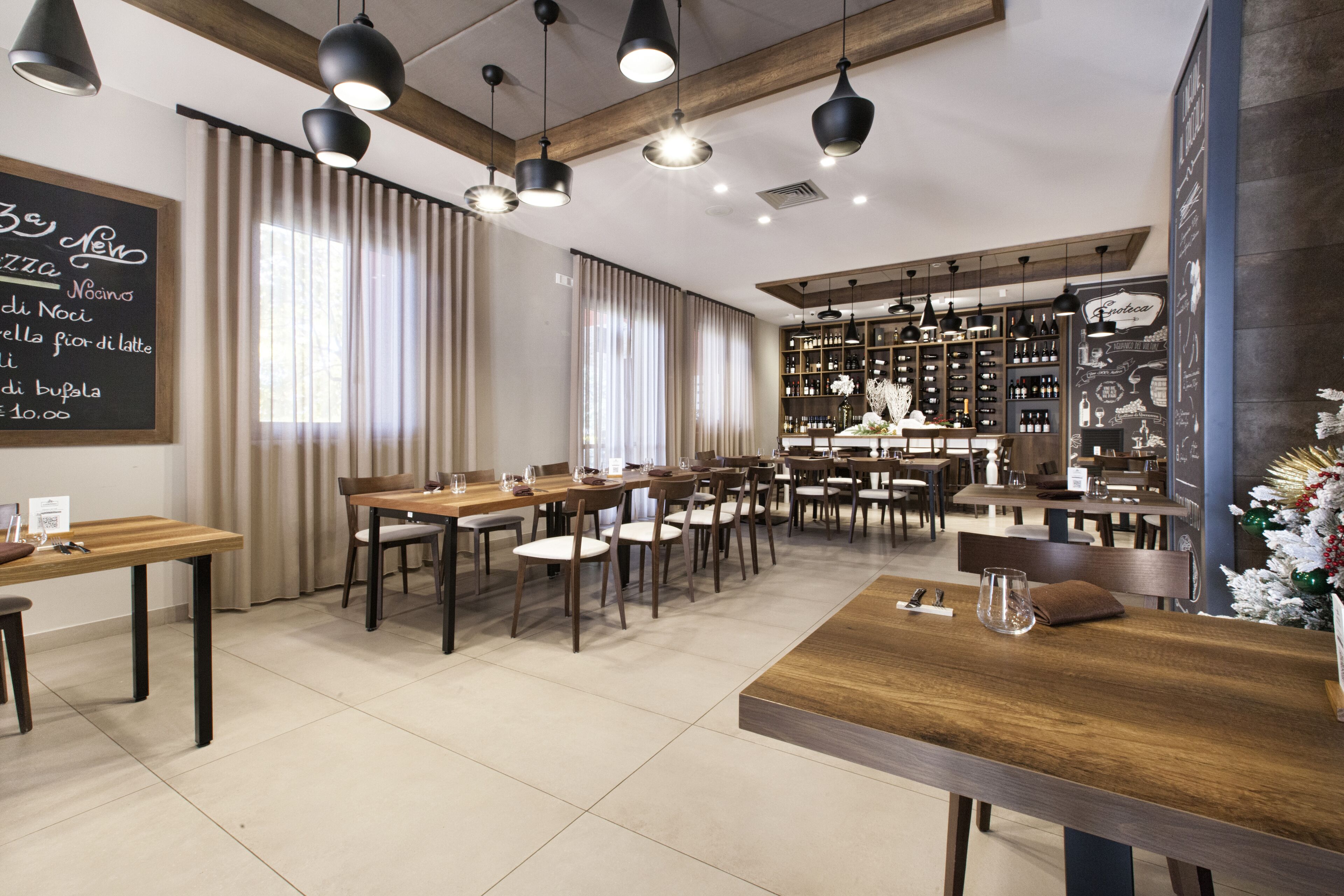 A restaurant with multiple tables and chairs, a bar area with shelves of bottles, and a chalkboard menu on the wall.