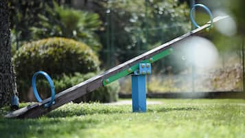 A seesaw with blue rings, set in a grassy area with trees and a fence in the background.