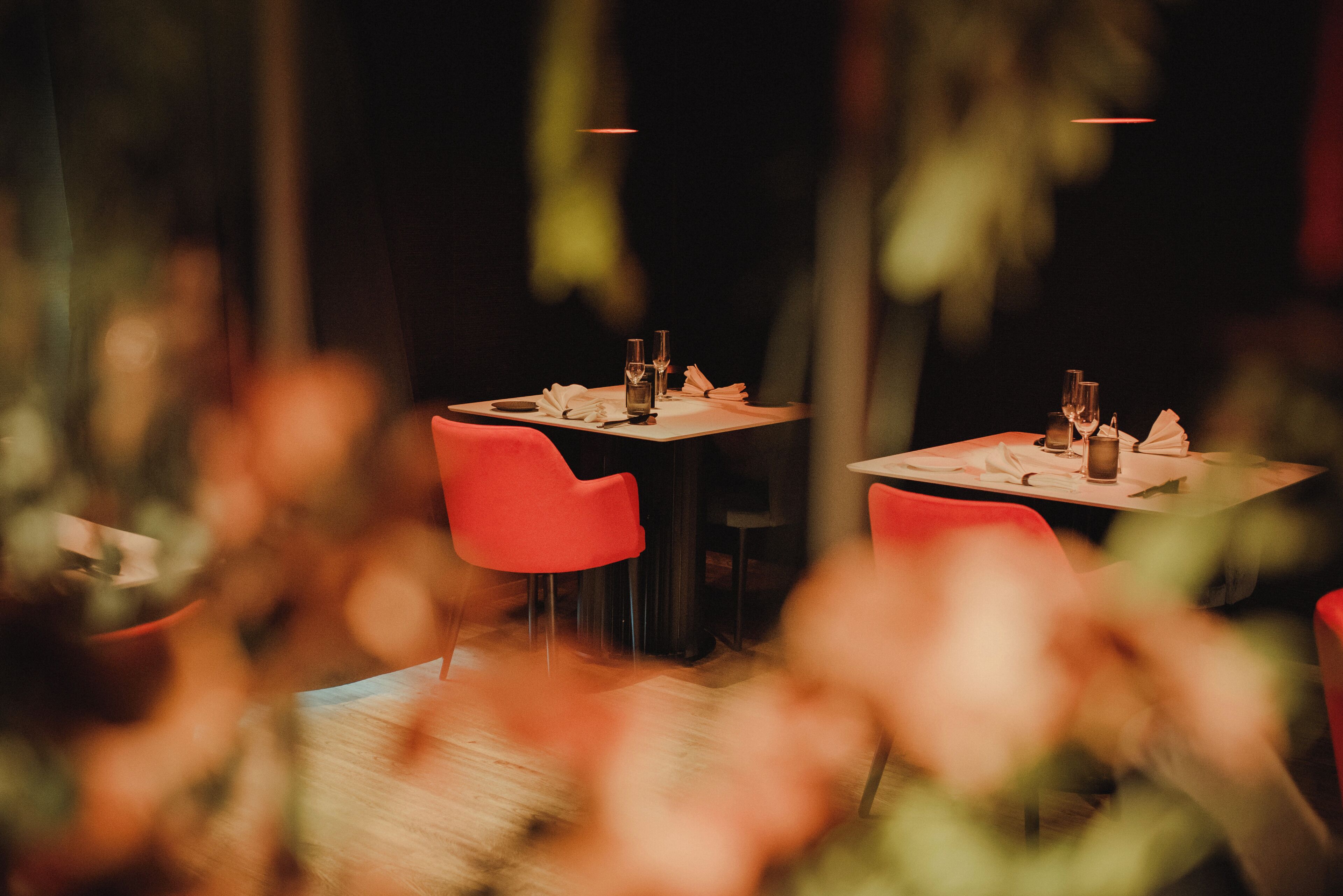 A restaurant with tables set for dining, red chairs, and a dimly lit ambiance.