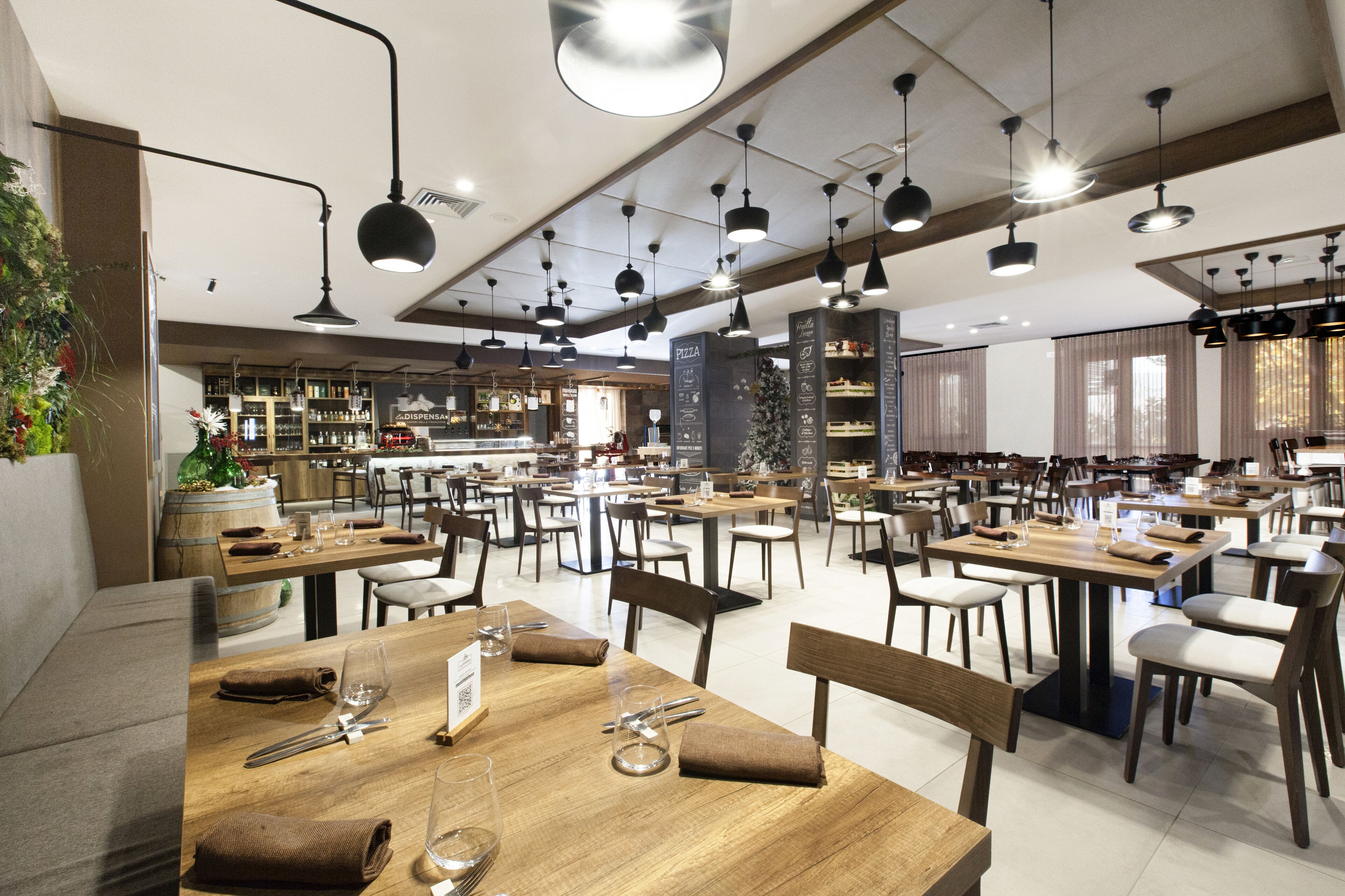 Een ruime restaurantruimte met meerdere eettafels en stoelen, een bar en diverse hanglampen.