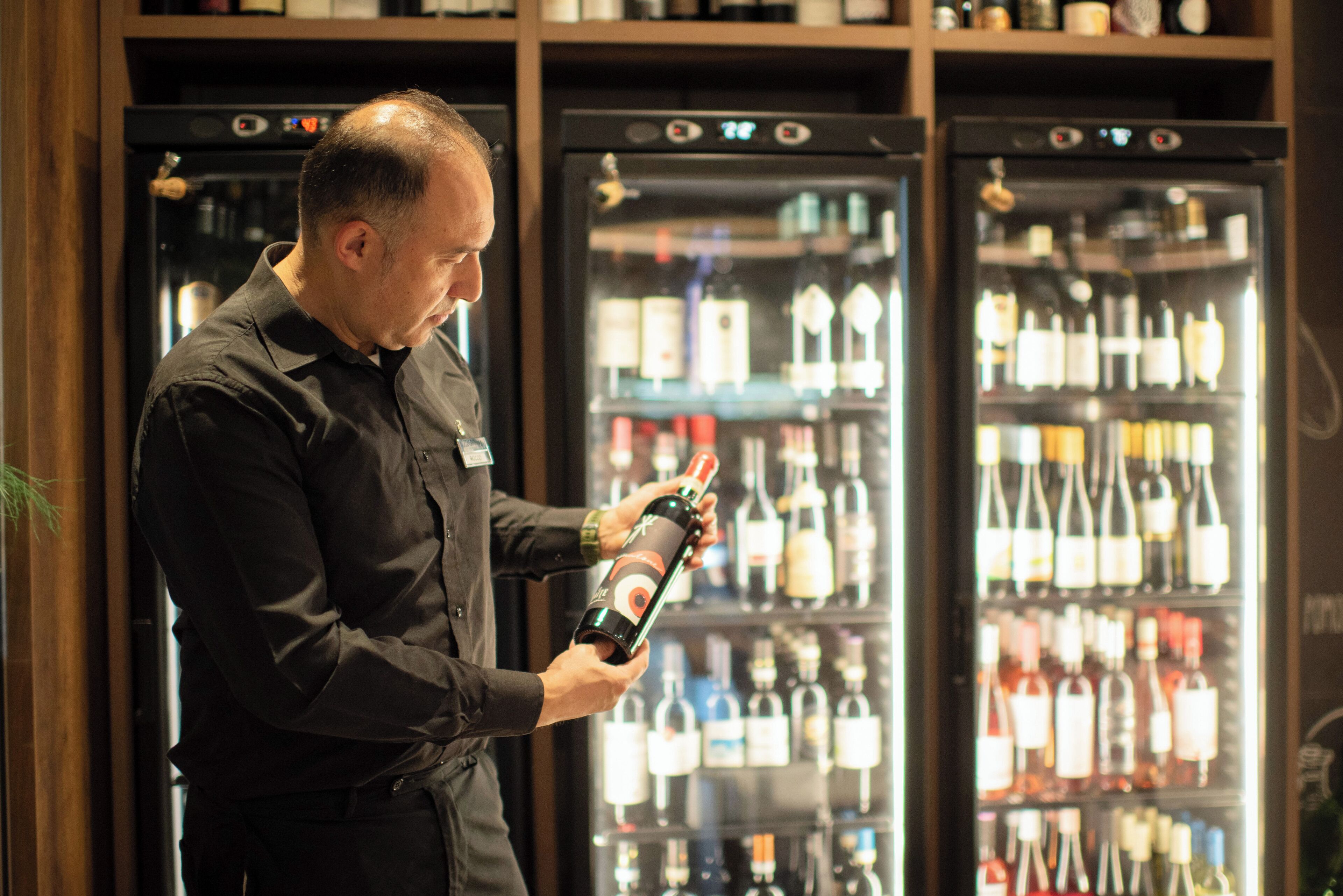 Iemand houdt een fles vast voor een koelkast vol met verschillende flessen.