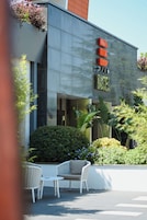 A modern hotel exterior with a glass facade, a sign reading "HOTEL", and outdoor seating.