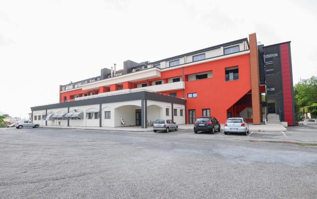A modern building with a red facade, multiple levels, and a parking lot with several cars.