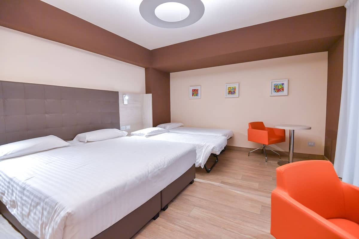 Una habitación de hotel con dos camas, una mesita, una silla y cuadros en las paredes.