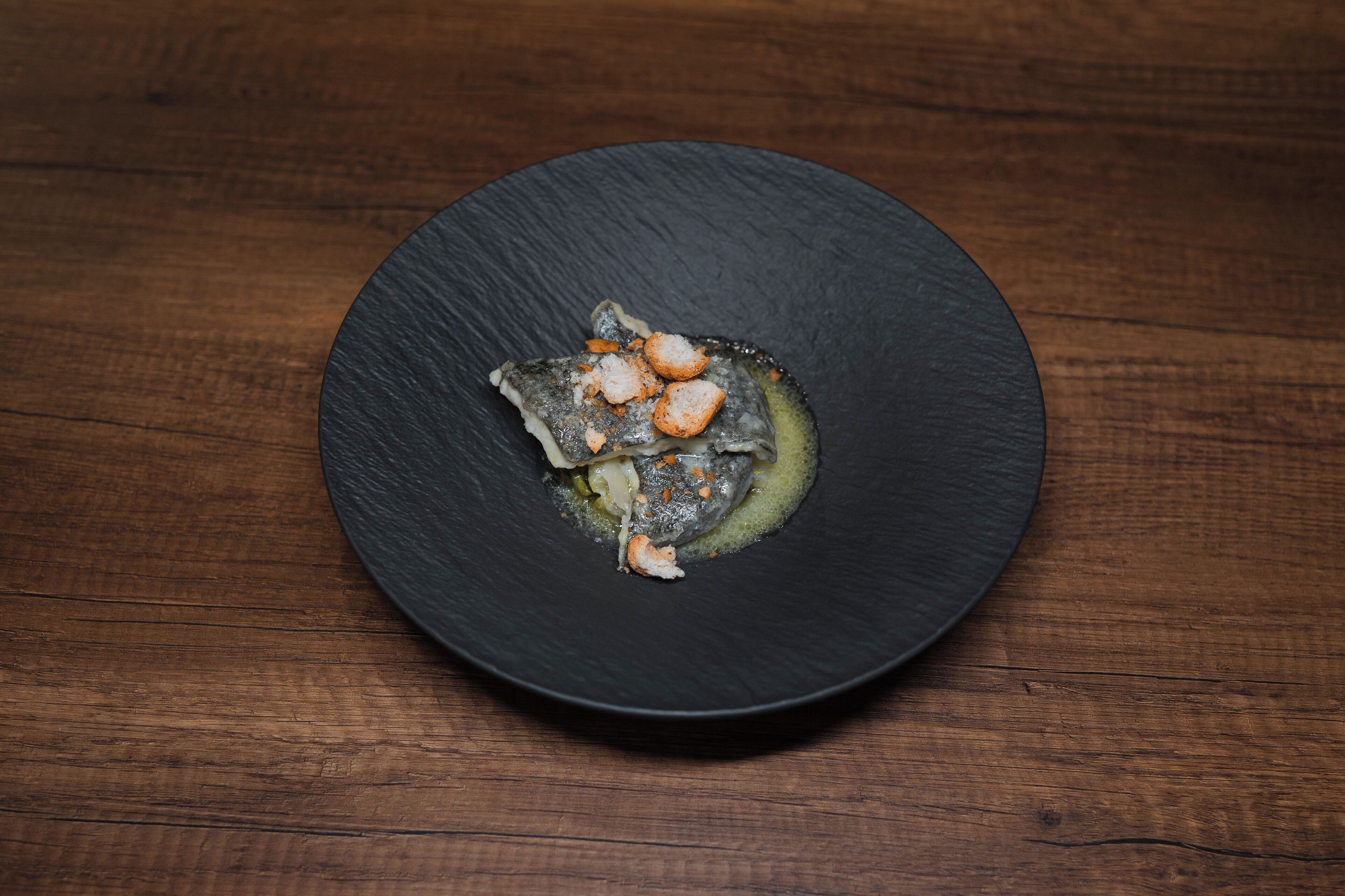 A black plate with a seafood dish on a wooden table.