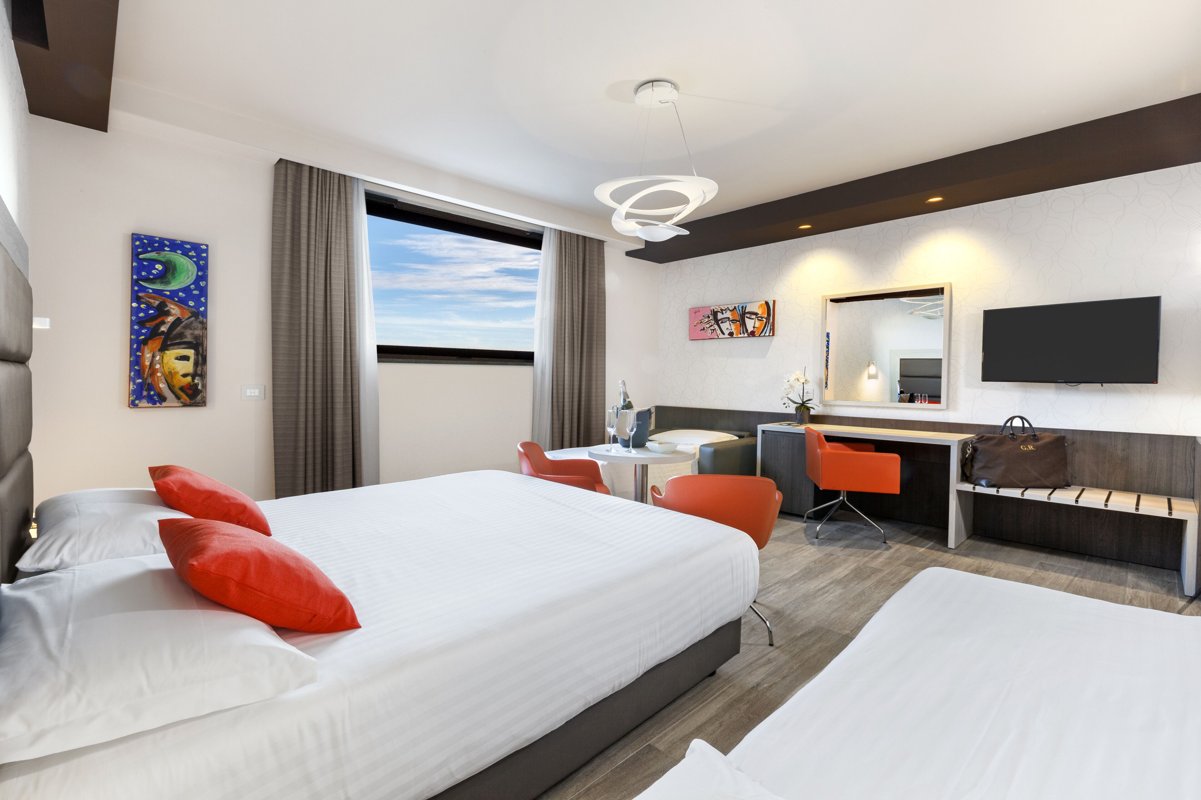 Una habitación de hotel con una cama grande, un escritorio, una silla, un televisor y obras de arte en las paredes.