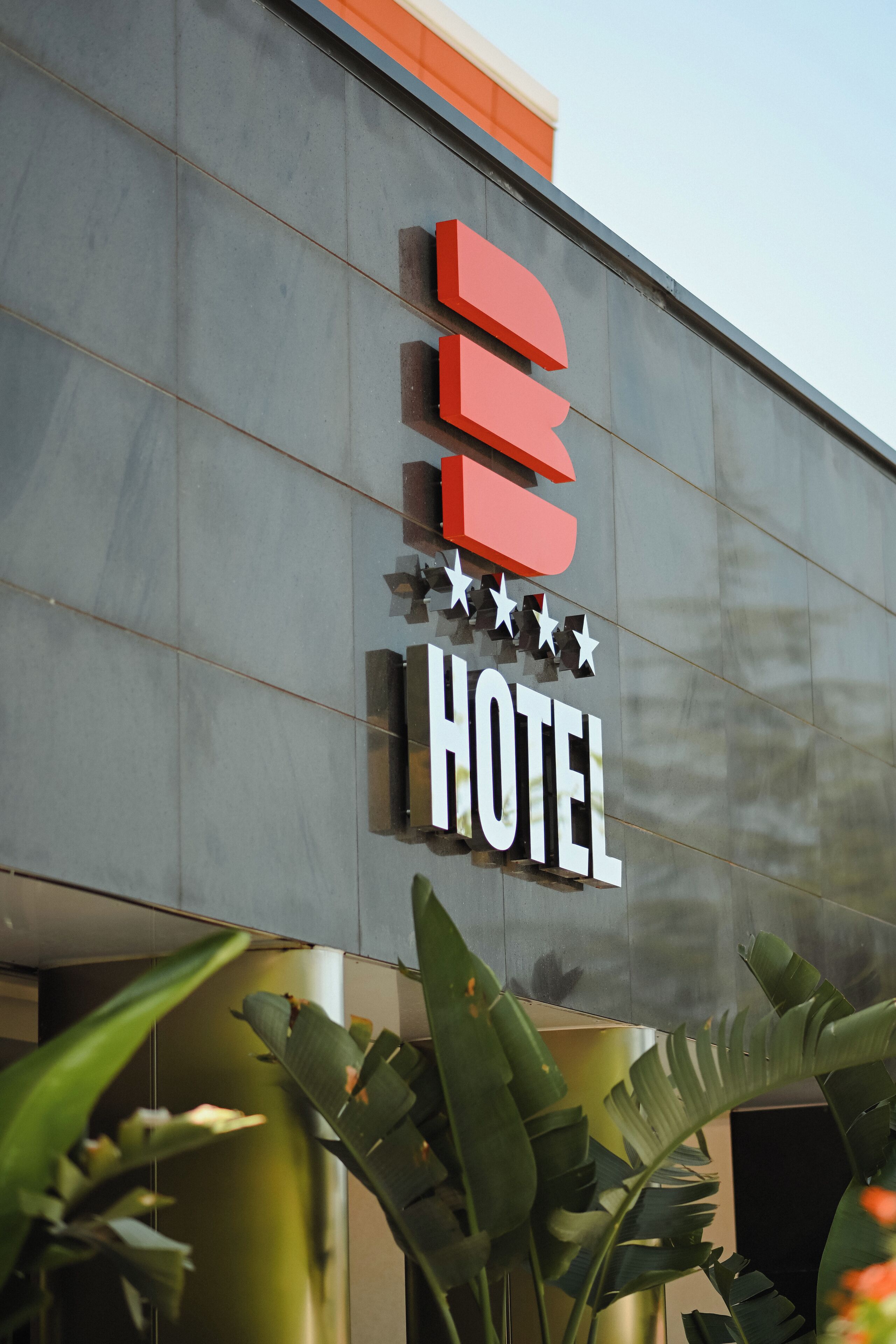 Un letrero de hotel con diseño moderno, que muestra tres letras rojas y cinco estrellas encima de la palabra 'HOTEL'.