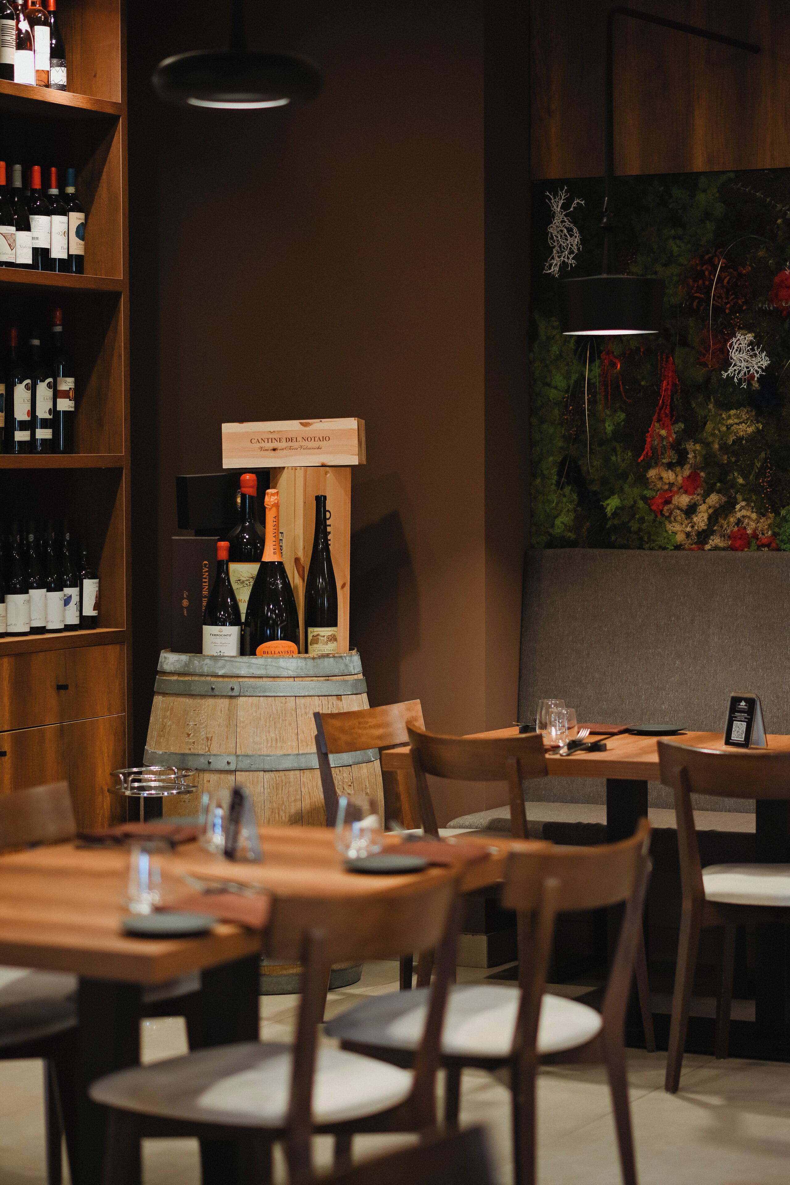 Un interior de restaurante con mesas y sillas de madera, una exhibición de vinos y una pared decorativa.