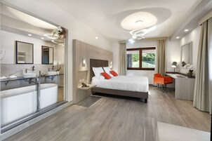 A modern hotel room with a large bed, a desk, a chair, a bathroom with a bathtub, and a large window with curtains.
