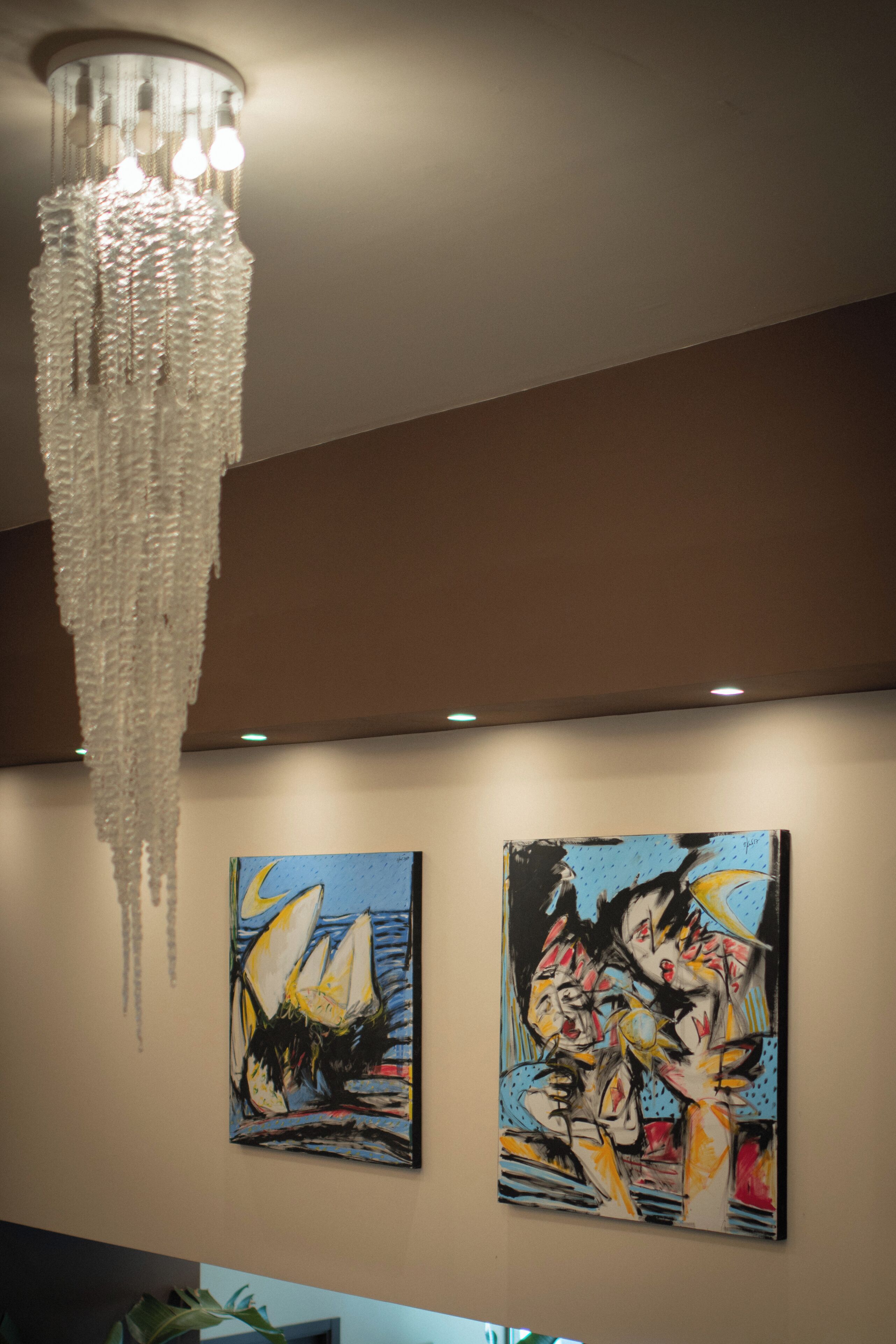 A chandelier hanging from the ceiling, two paintings on the wall, and a plant in the foreground.