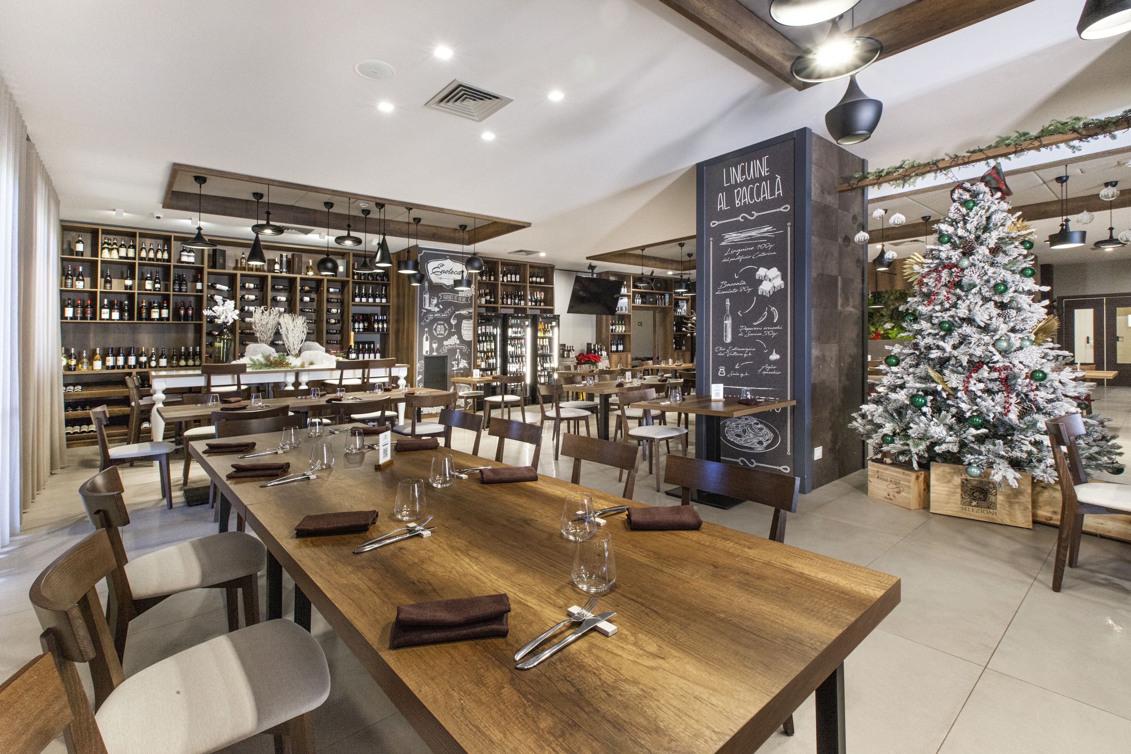 A restaurant with wooden tables and chairs, a Christmas tree, and shelves of bottles.