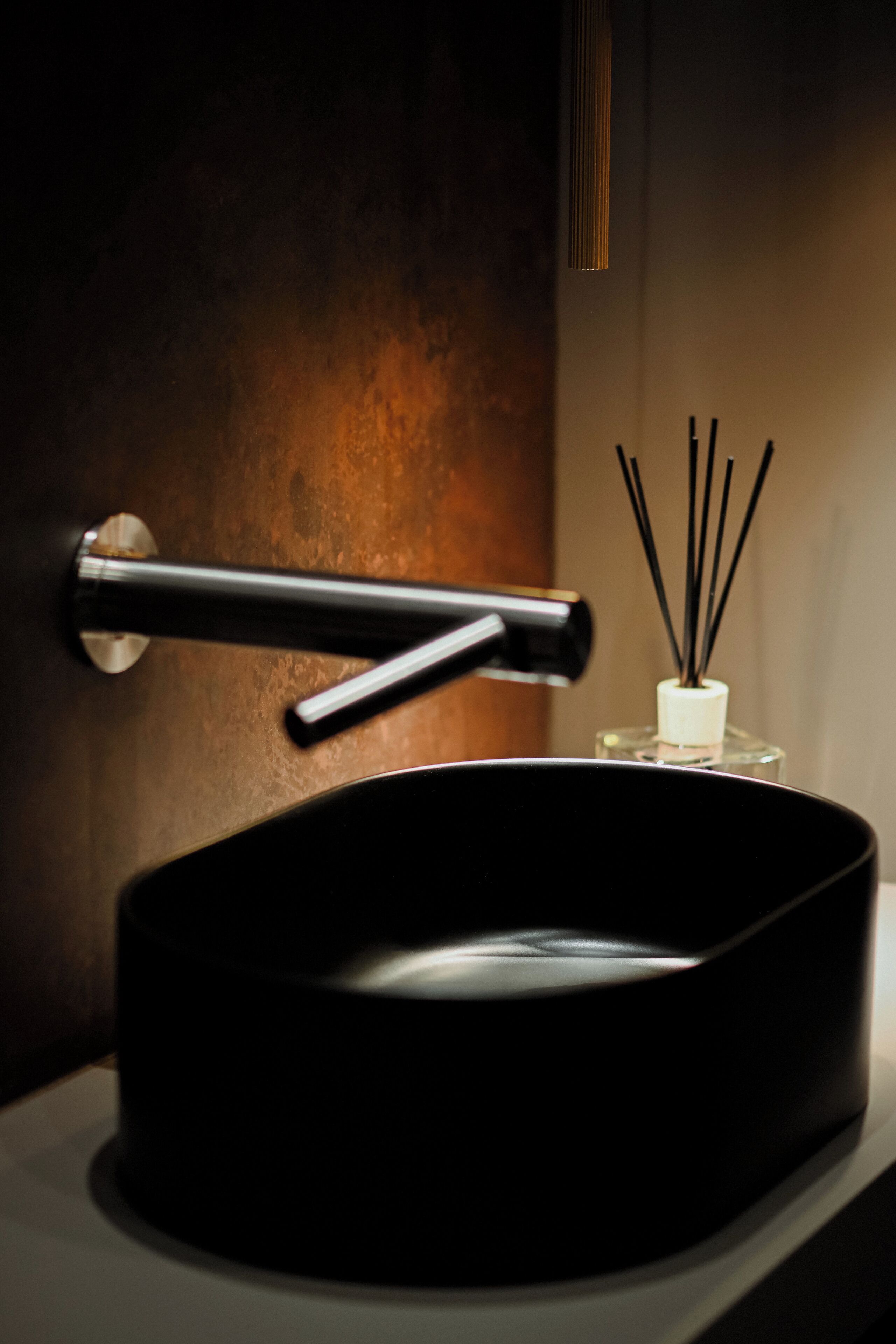 Un lavabo negro con un grifo moderno y un pequeño recipiente blanco con difusores de caña.