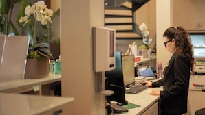 A woman working at a desk with a computer, surrounded by office supplies and potted plants. - BHotel (Lagonegro)