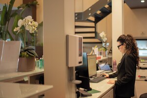 A woman working at a desk with a computer, surrounded by office supplies and potted plants.