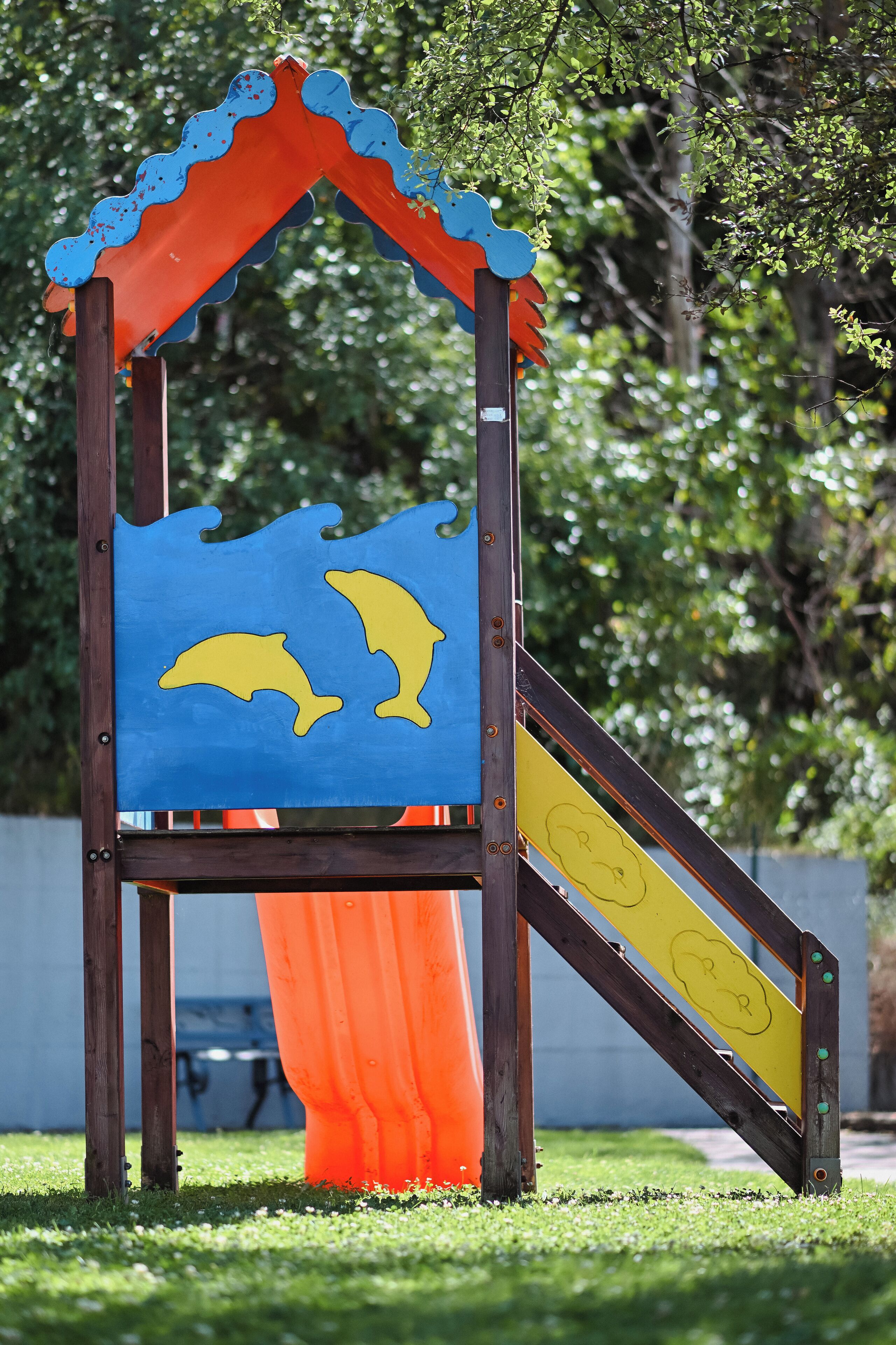 A wooden play structure with a slide and dolphin designs.