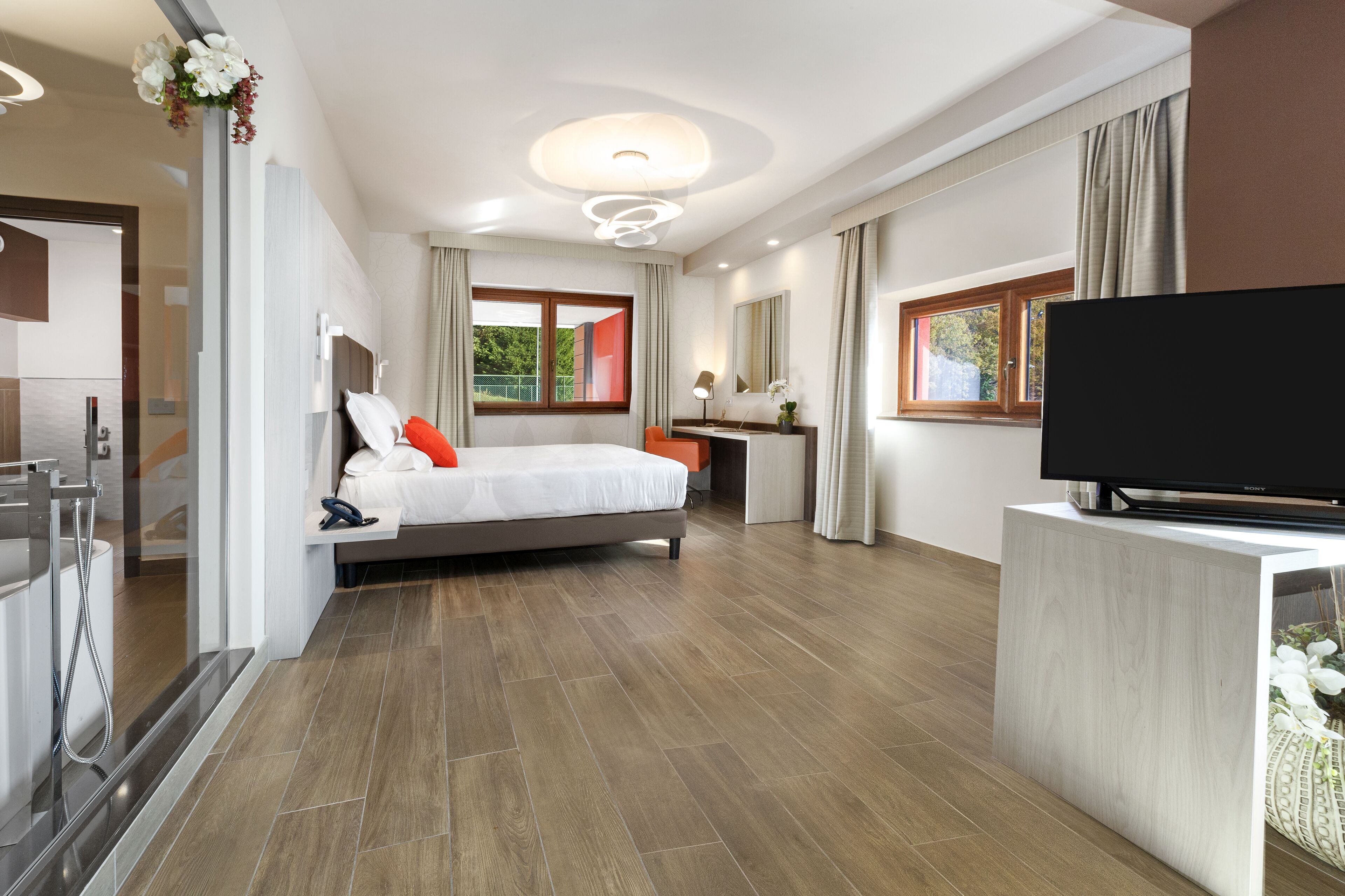 A modern hotel room with a large bed, a TV, a desk, and a bathroom with a shower.