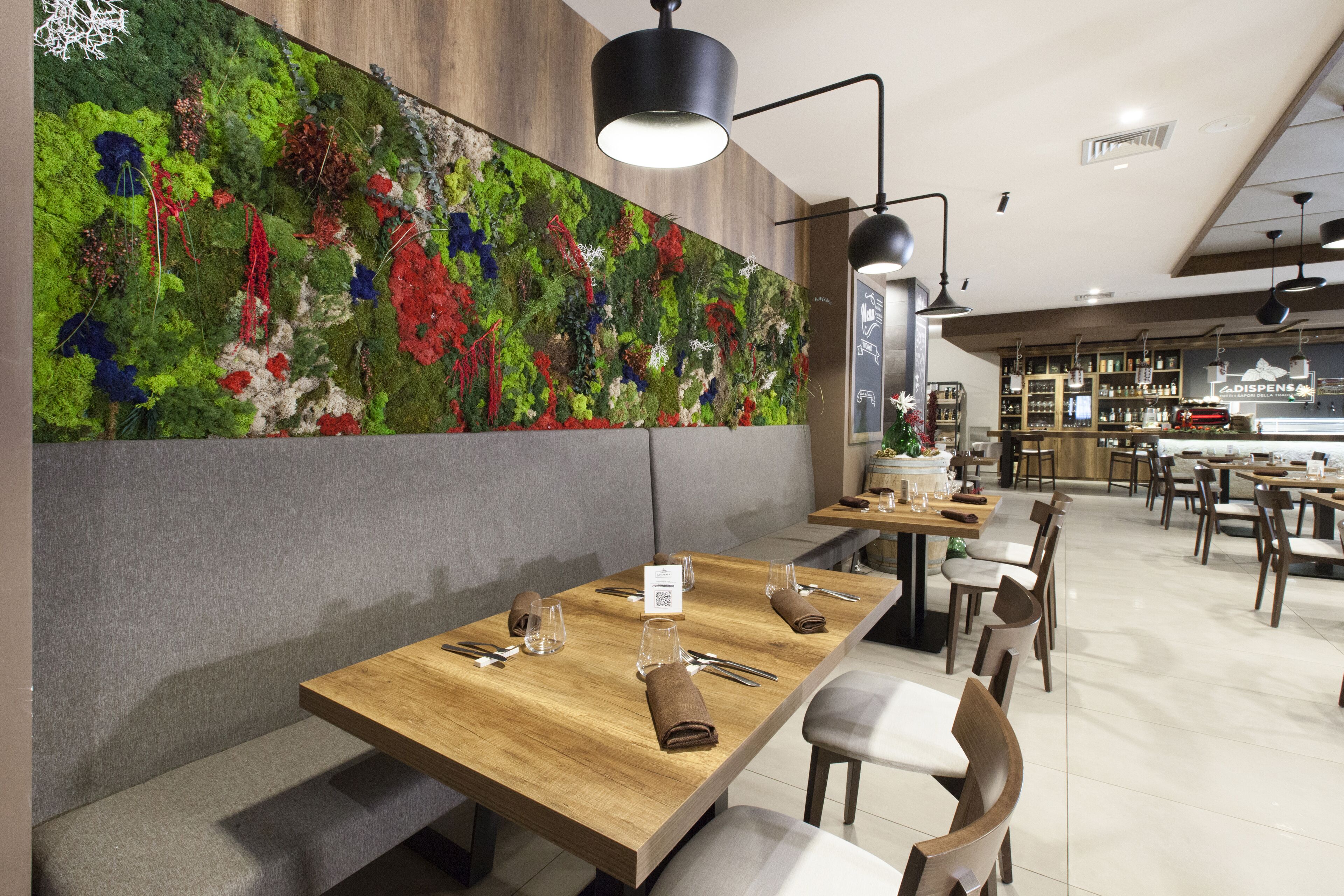 A restaurant with wooden tables, grey cushioned seating, and a colorful moss wall.