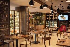 A restaurant with wooden tables and chairs, a wine cooler, and a television screen displaying food.
