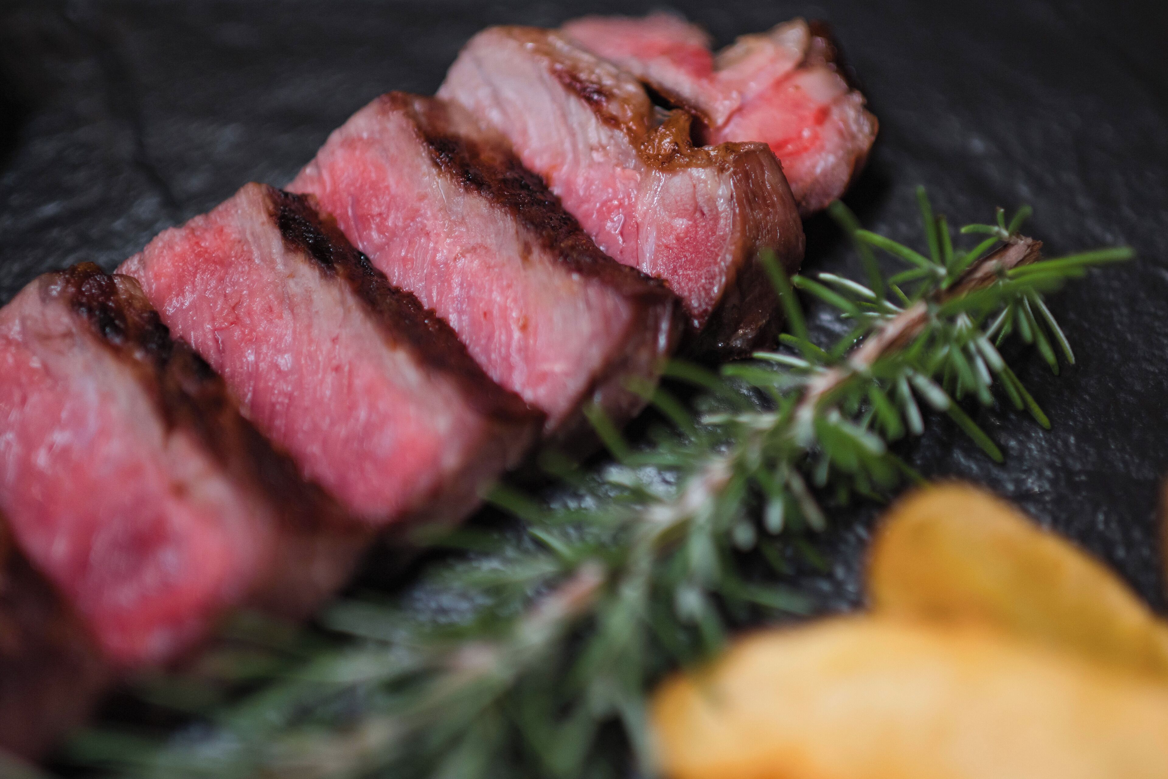 Primer plano de carne cortada en rebanadas con una guarnición de hierbas verdes.