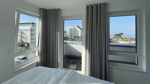 Una camera d'albergo con un letto, due finestre e vista su edifici e mare.