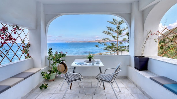 A balcony with a table and chairs, a view of the sea, and potted plants. - Blue Comfort Apartments Sitia (Sitia)
