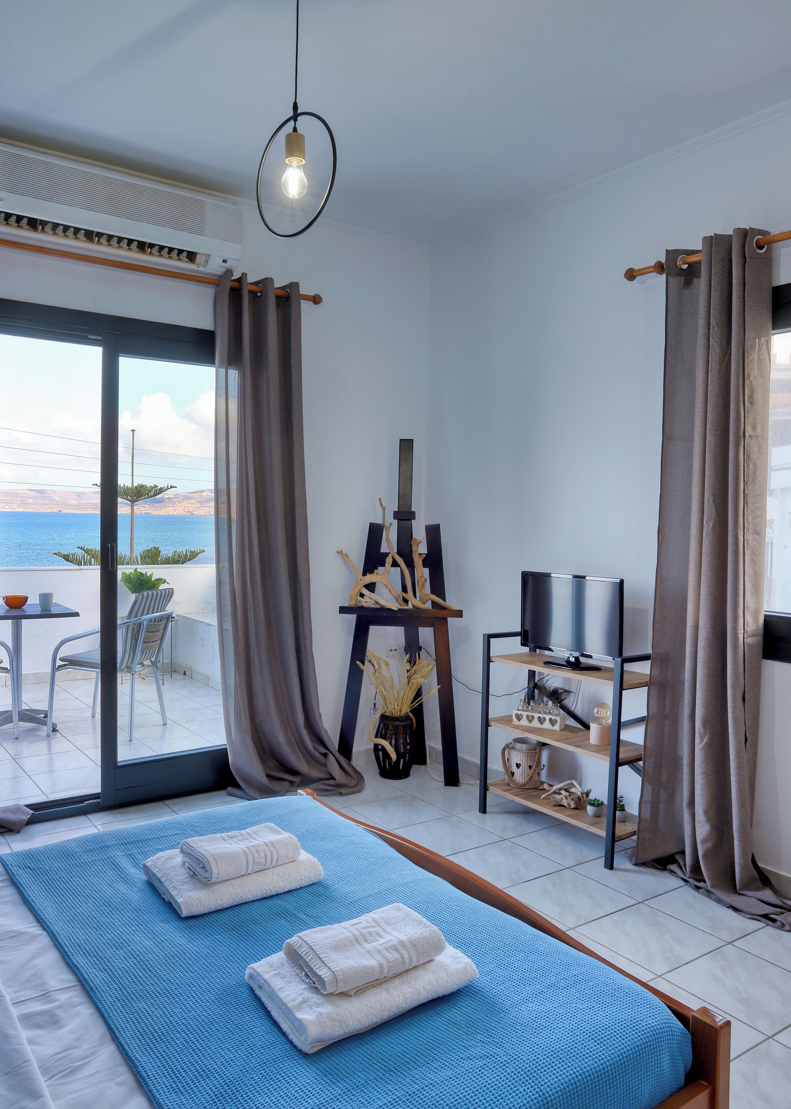 A modern bedroom with a large bed, a TV, and a view of the sea.