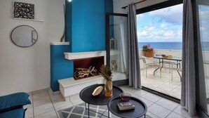 A modern living room with a blue accent wall, a fireplace, a dining area with a view of the sea, and a balcony with a table and chairs. - Blue Comfort Apartments Sitia (Sitia)