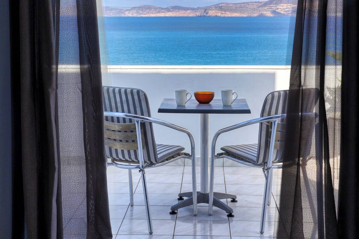 Un balcón con mesa y sillas, con vista a una masa de agua y tierra a lo lejos.