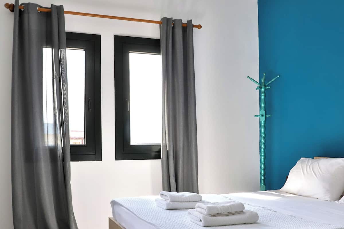 Habitación de hotel con una cama, cortinas grises, un banco de madera y una pared azul decorativa.