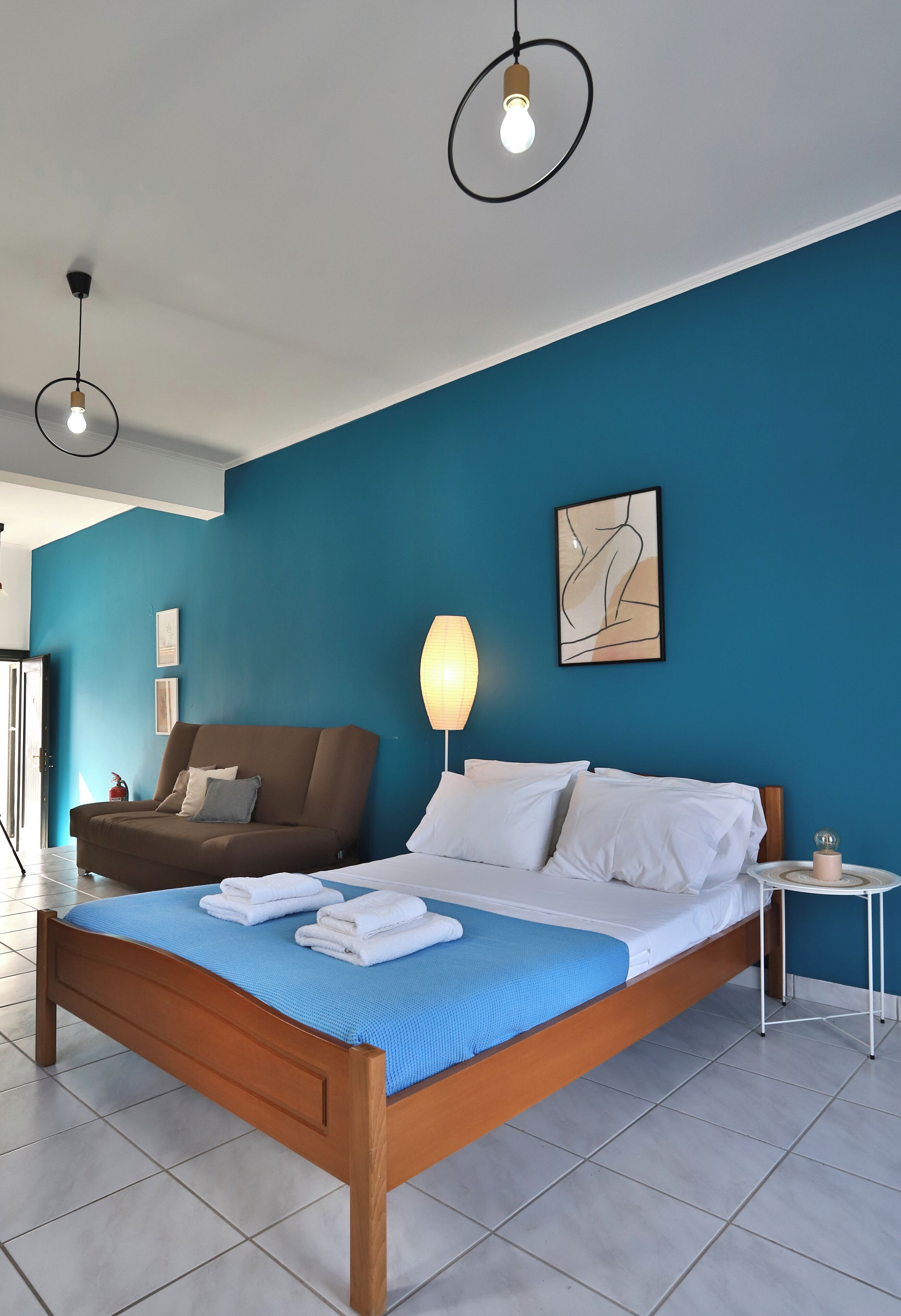 A bedroom with a bed, a sofa, a lamp, and a painting on the wall.